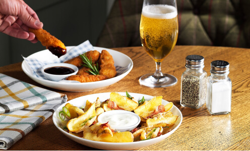 A table with two Brewers Fayre starters, including chicken goujons and potato dippers with a small beer and salt and pepper shakers.