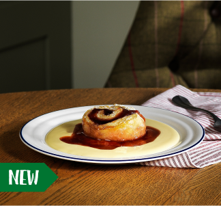Brewers Fayre Jam Roly Poly in the middle of a round plate with red jam and custard.