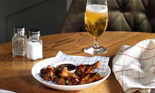 Brewers Fayre chicken wings with a BBQ dip in a white dish next to a small beer and salt and pepper shakers.
